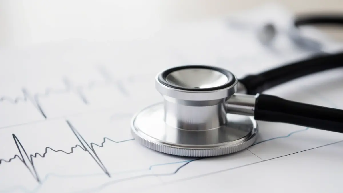 Image générique d'un stéthoscope sur un dossier médical flou avec des lignes de rythme cardiaque abstraites.